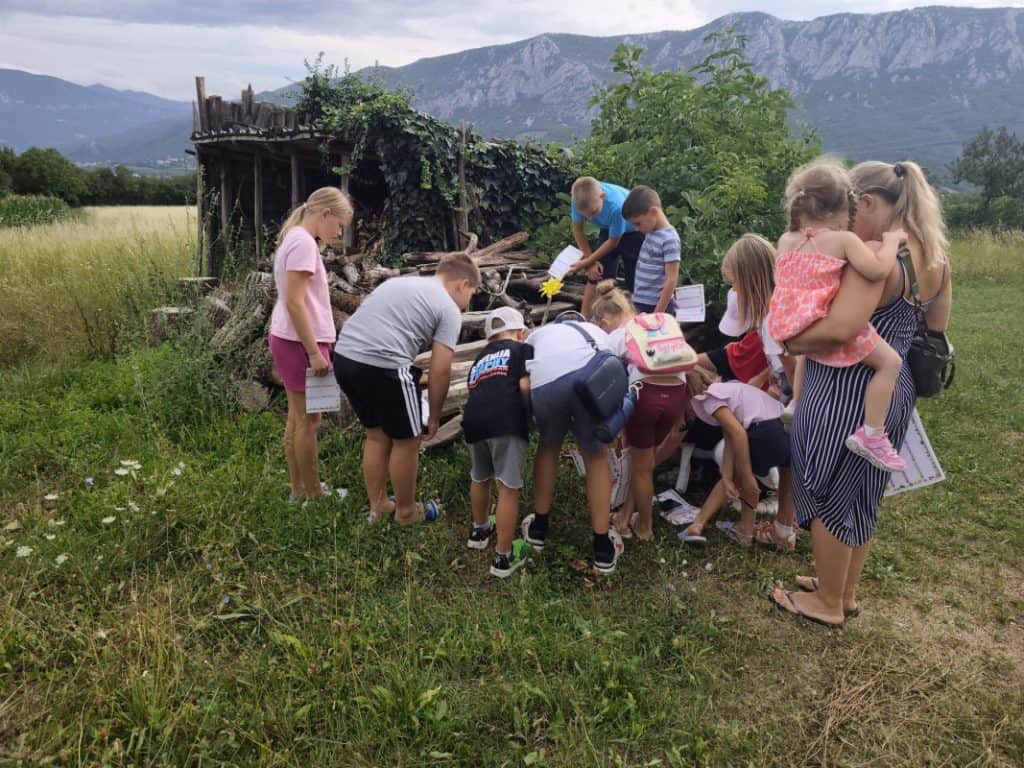 Skupina otrok podrobno gleda v tla, kjer so žuželke.